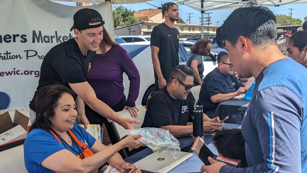 Student athletes Clark Slajchert (foreground) and Matt Knowling (background) assist PHFE WIC staff in handing out free children's books. Photo by Heluna Health.